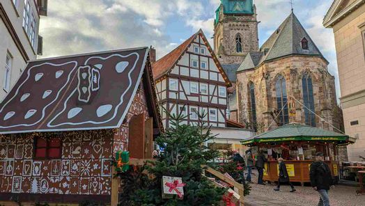 Zu sehen ist das Lebkuchenhaus auf dem Weihnachtsmarkt in Bad Wildungen am Tage. Im Hintergrund ist ein Fachwerkhaus sowie die Stadtkirche zu sehen.