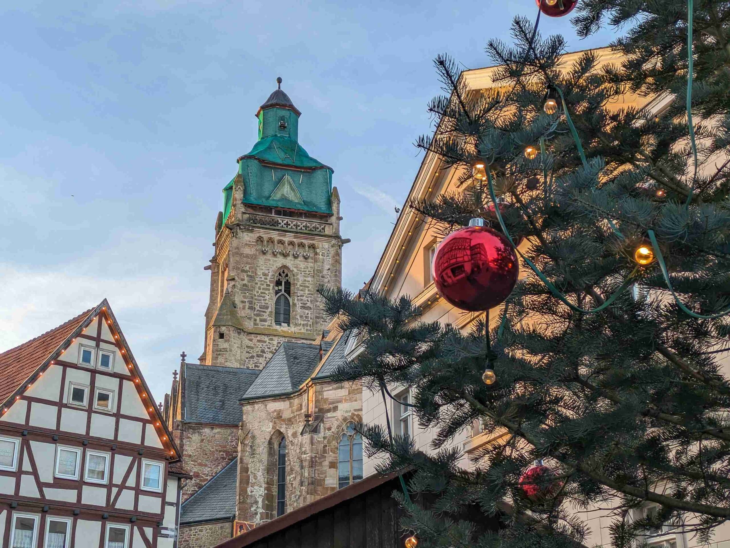 Zu sehen ist ein Fachwerkhaus und die Bad Wildunger Stadtkirche davor ein Teil der Weihnachtsbaums und einer roten Kugel.