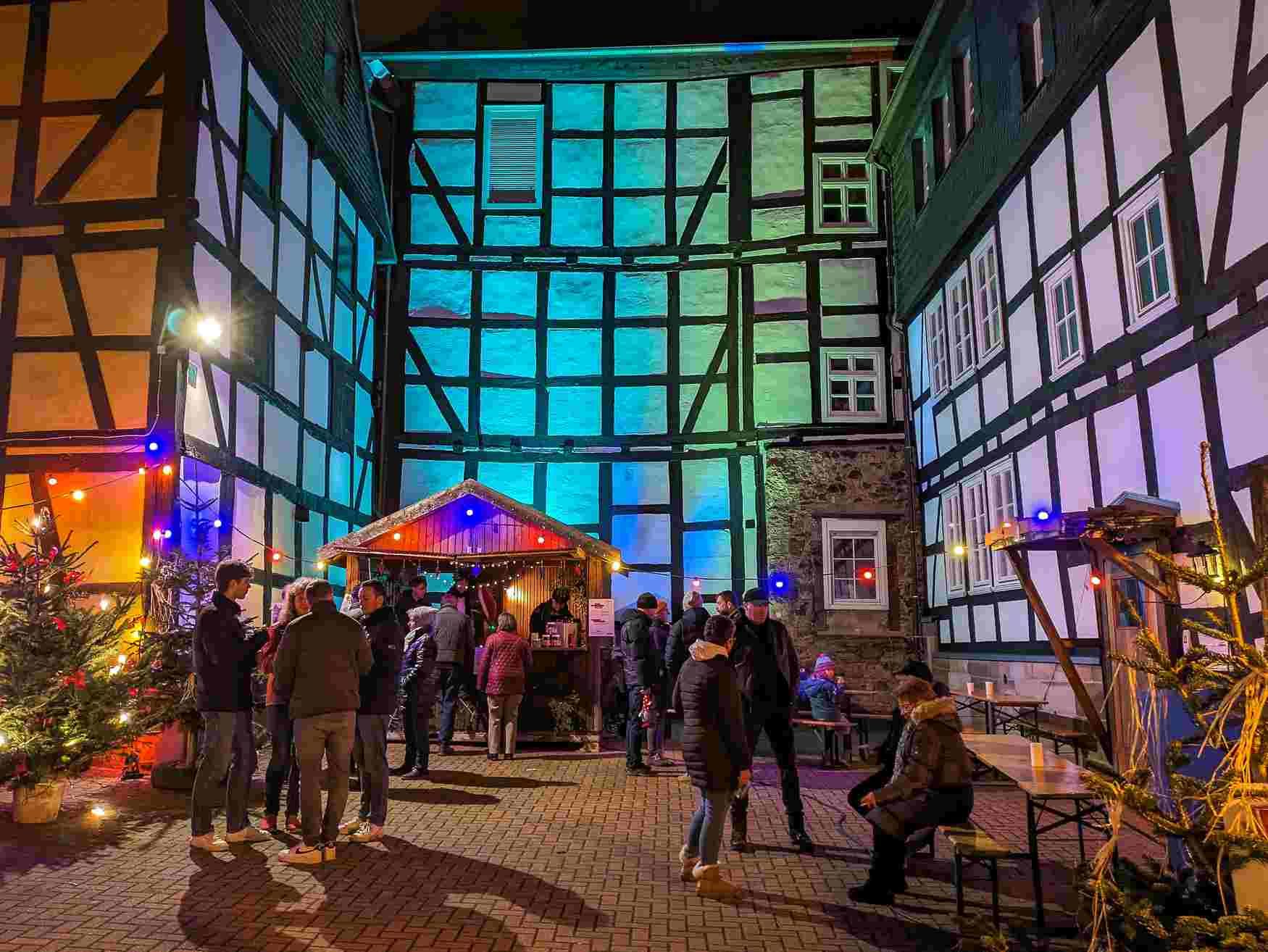 Menschen auf dem Weihnachtsmarkt in der Dunkelheit. Im Hintergund angestrahlte Fachwerkhäuser.
