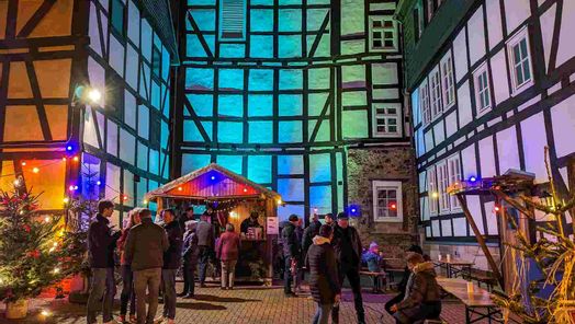 Menschen auf dem Weihnachtsmarkt in der Dunkelheit. Im Hintergund angestrahlte Fachwerkhäuser.