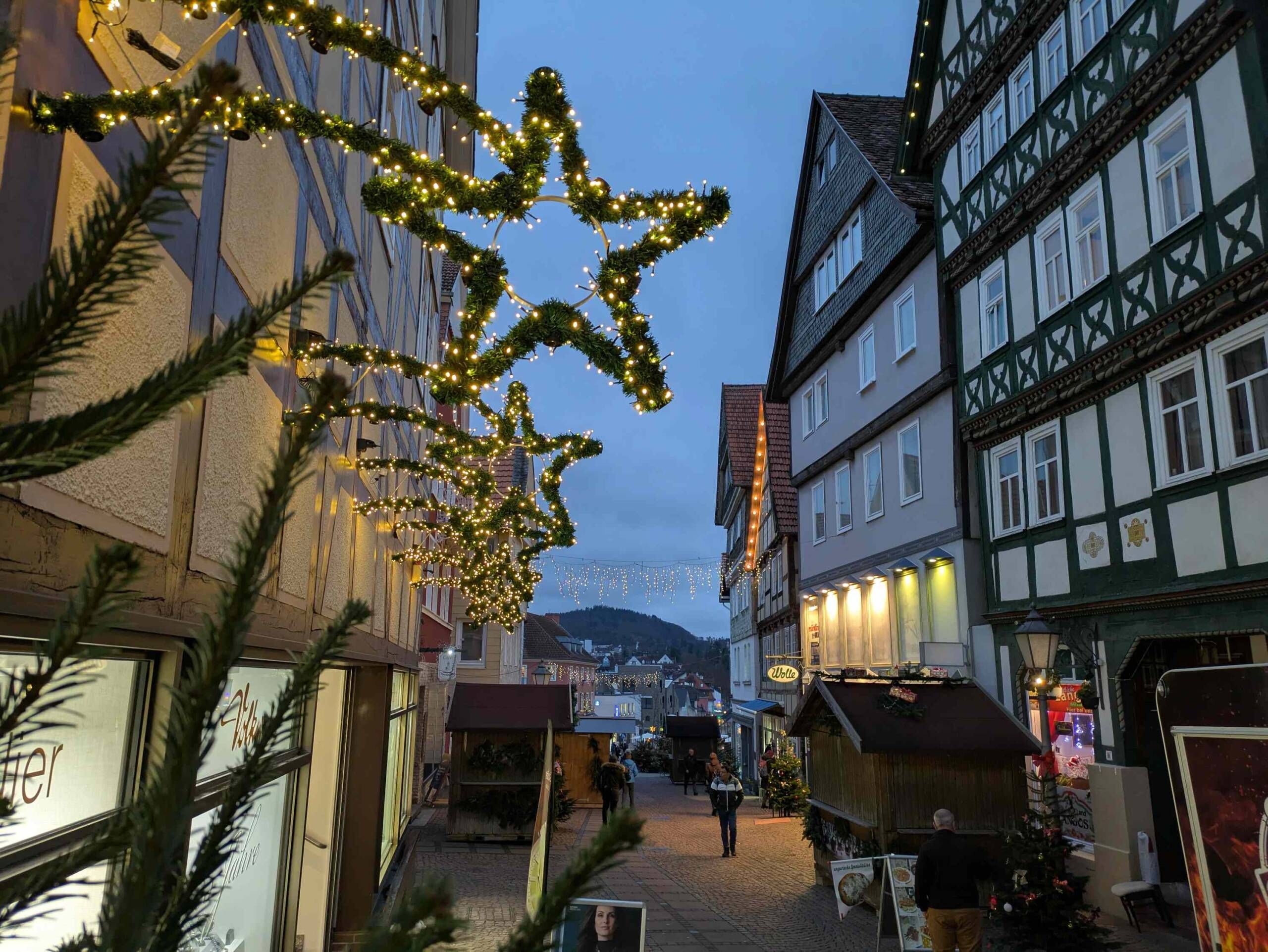 Zu sehen ist die Brunnenstraße in der Altstadt in Richtung Marktplatz schauend bei Dämmerung. Links hängt weihnachtliche Dekoration an den Häusern und rechts sieht man ein paar Stände vor den Fachwerkhäusern.