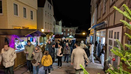 Zu sehen sind Menschen auf den Weihnachtsmarkt in der Brunnenstraße. Rechts und links an den Fachwerkhäusern stehen Stände.