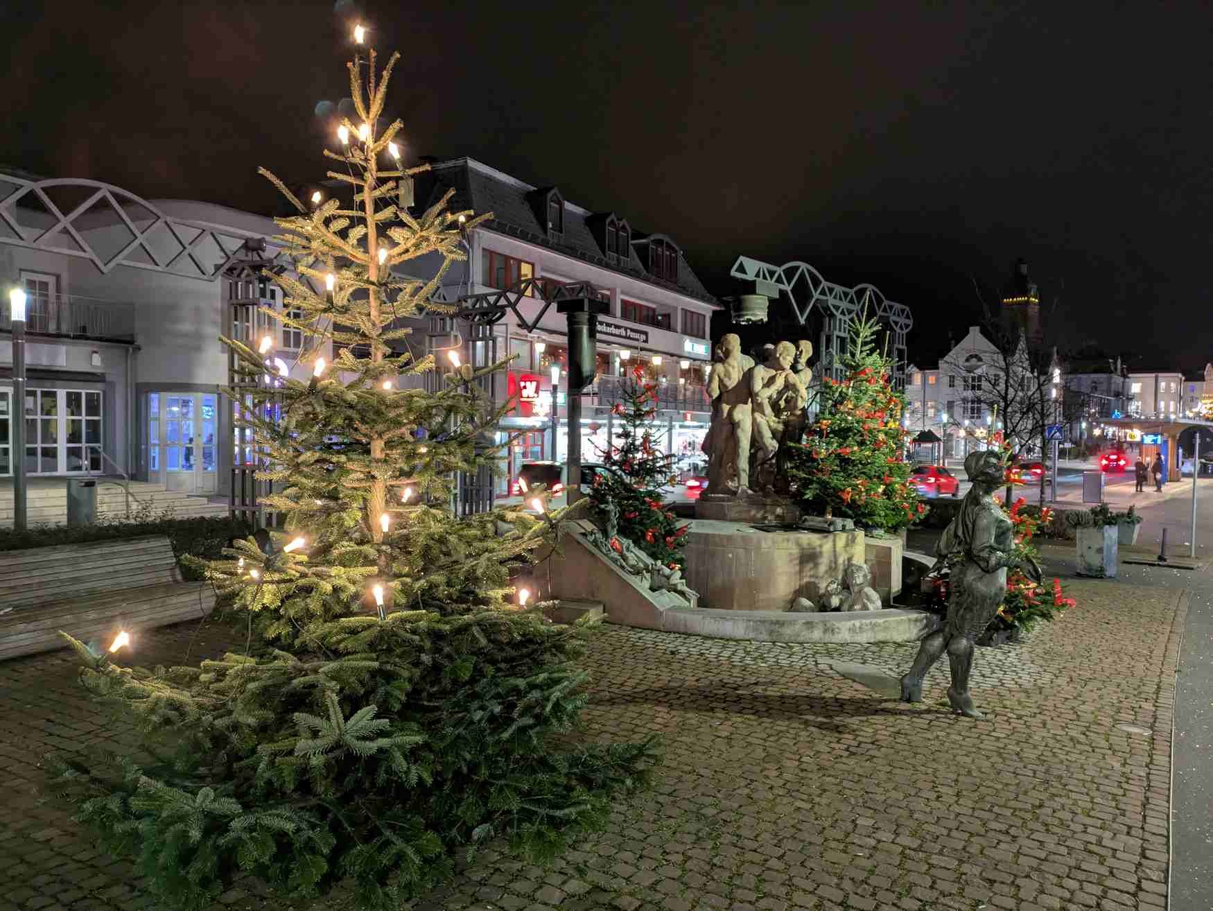 Zu sehen ist der mit Weihnachtsbäumen geschmückte Kurschattenbrunnen in der Dunkelheit.