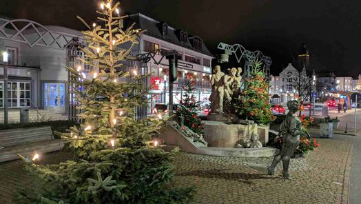 Zu sehen ist der mit Weihnachtsbäumen geschmückte Kurschattenbrunnen in der Dunkelheit.