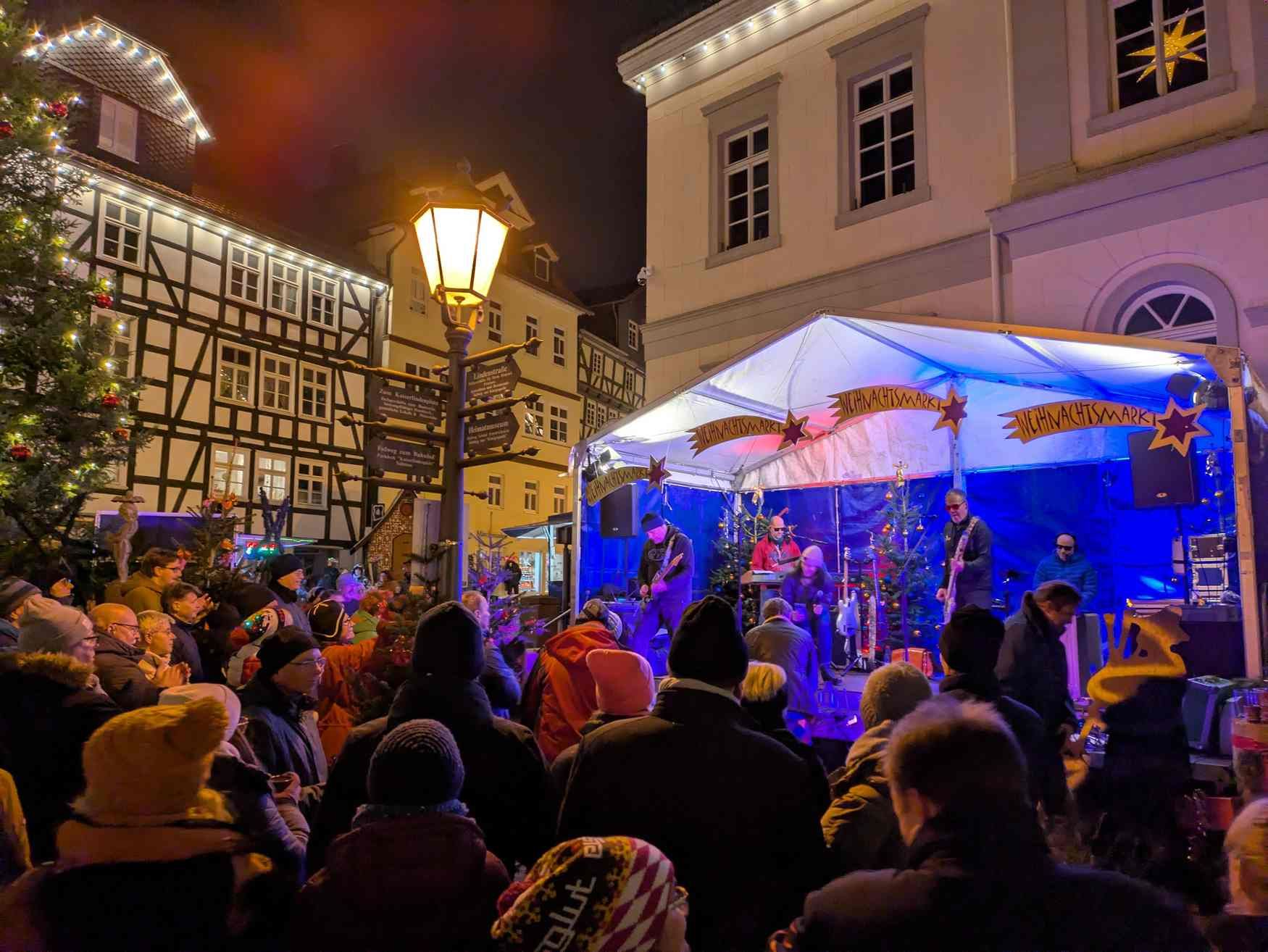 Zu sehen sind Menschen vor einer Bühne, die vor dem Rathaus steht am Abend.