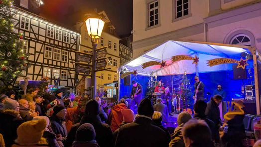 Zu sehen sind Menschen vor einer Bühne, die vor dem Rathaus steht am Abend.