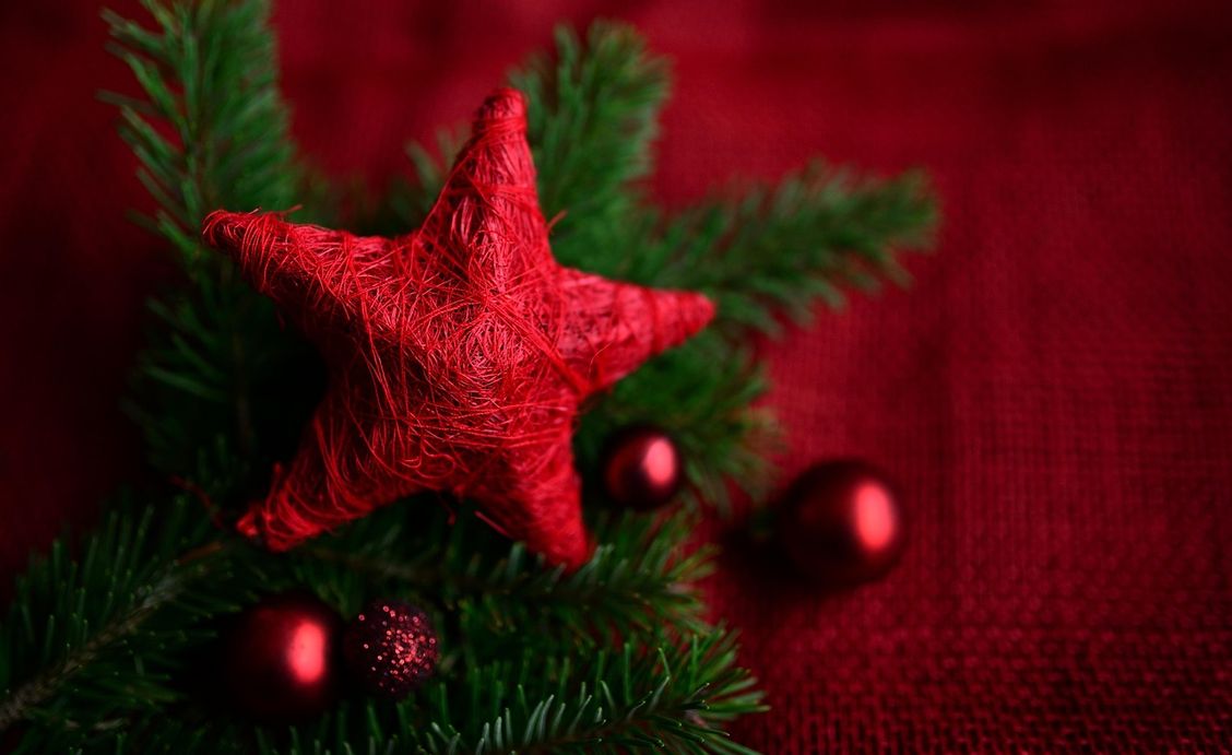 Zu sehen sind ein paar grüne Tannenzweige, ein roter Stern sowie rote Weihnachtskugeln vor rotem Hintergrund.