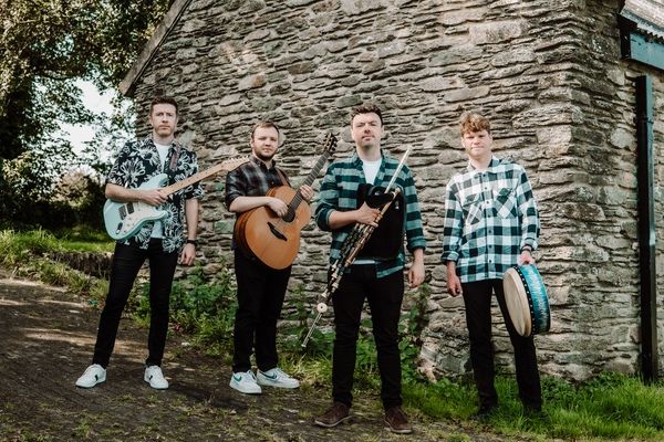 Zu sehen ist die vier-köpfige Conor Mallon Band mit ihren Musikinstrumenten in der Hand vor einem steinernen Gebäude. Im Hintergrund ist ein Baum zu sehen.