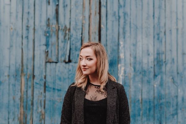 Zu sehen ist die Sängerin Iona Fyfe in schwarzer Kleidung vor einem blauen Hintergrund.