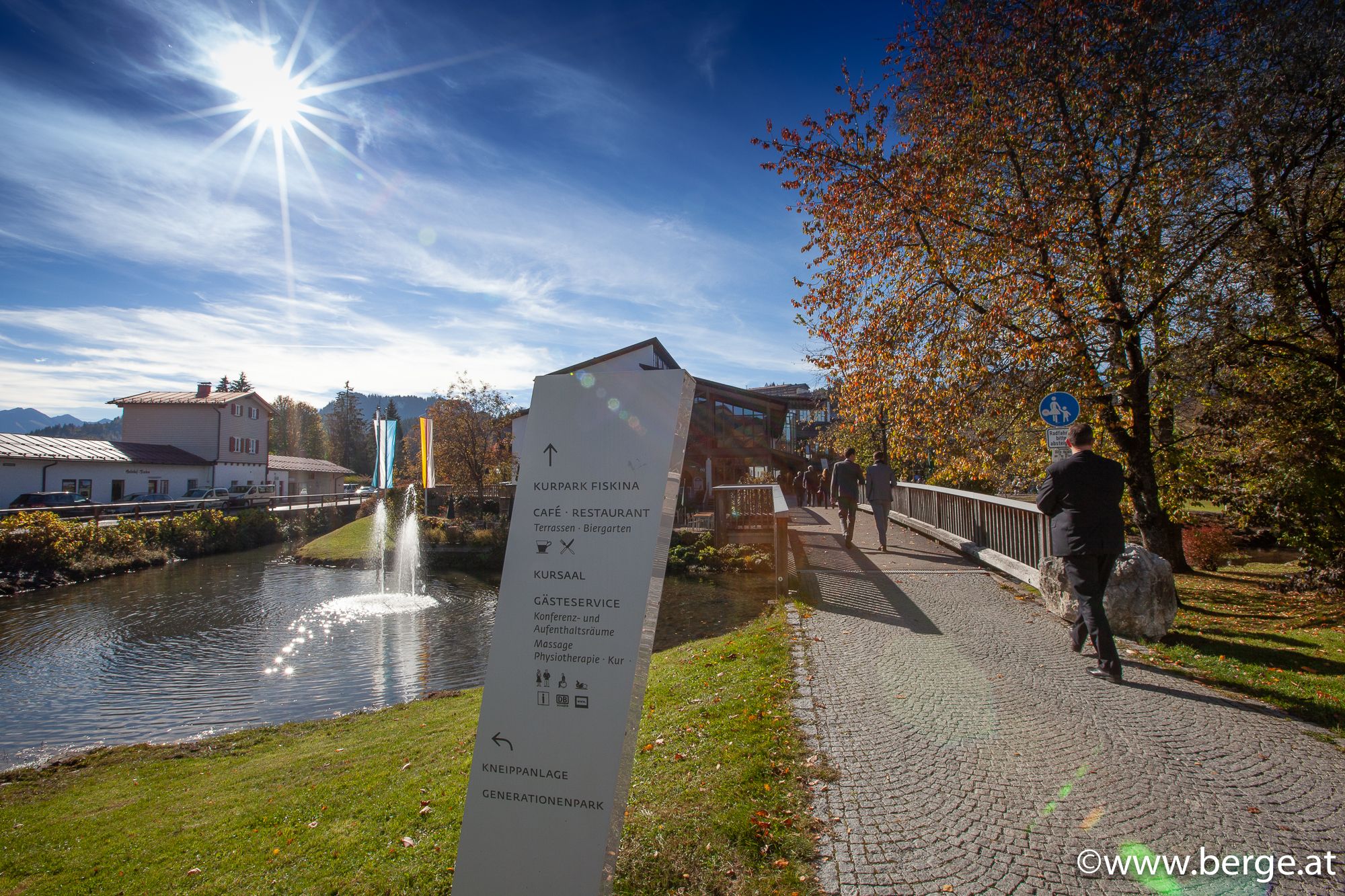 Ein Park mit einem sanft fließenden Fluss, umgeben von grünen Wiesen und Bäumen.