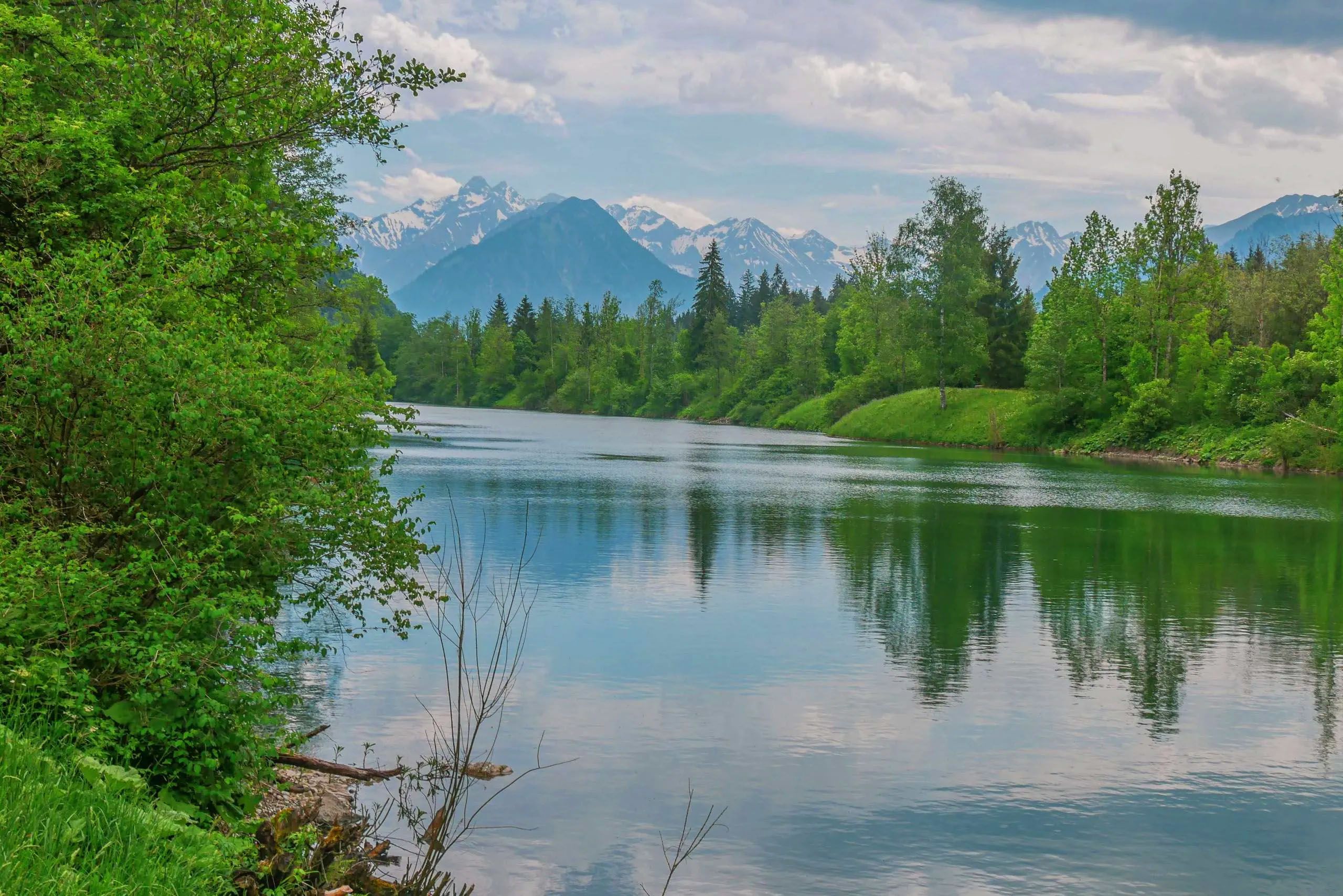 Kristallklarer Bach fließt vor einer beeindruckenden alpinen Landschaft mit grünen Wiesen und majestätischen Bergen im Hintergrund.
