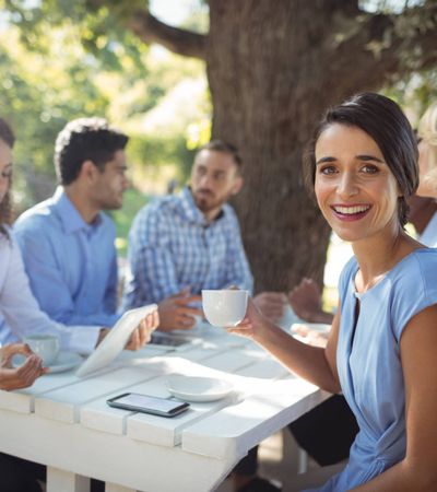 Porträt einer Frau, die mit Kollegen in einem Außenbereich eines Restaurants sitzt – geselliges Beisammensein und Genuss in entspannter Atmosphäre.