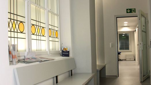Praxisflur mit Sitzbank und bunt verglastem Fenster