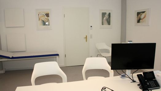 Sprechzimmer mit Tisch, Monitor und Telefon, drei Stühle