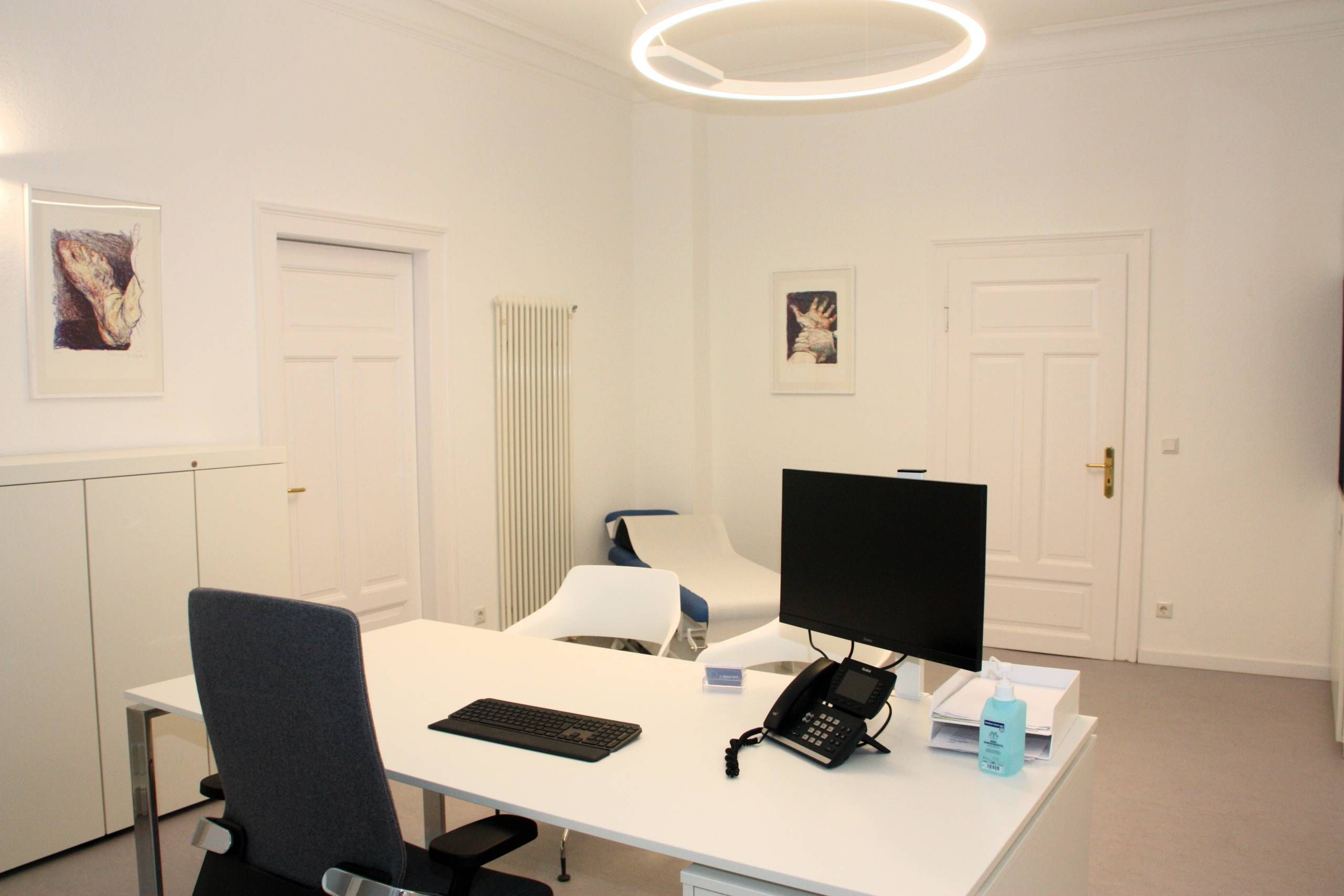 Sprechzimmer mit Tisch, zwei Stühle, Behandlungsliege, Monitor