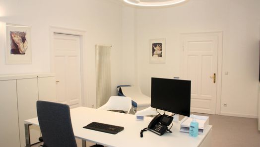 Sprechzimmer mit Tisch, zwei Stühle, Behandlungsliege, Monitor