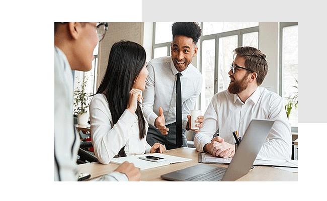 Vier gut gelaunte Personen sitzen oder stehen um einem Schreibtisch herum und diskutieren