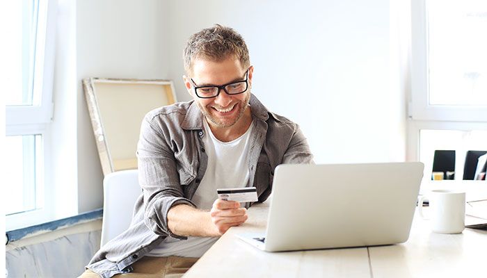 Kundenkontaktpunkt und NPSplus: Ein Mann sitzt am Laptop mit seiner Kreditkarte und kauft etwas online.