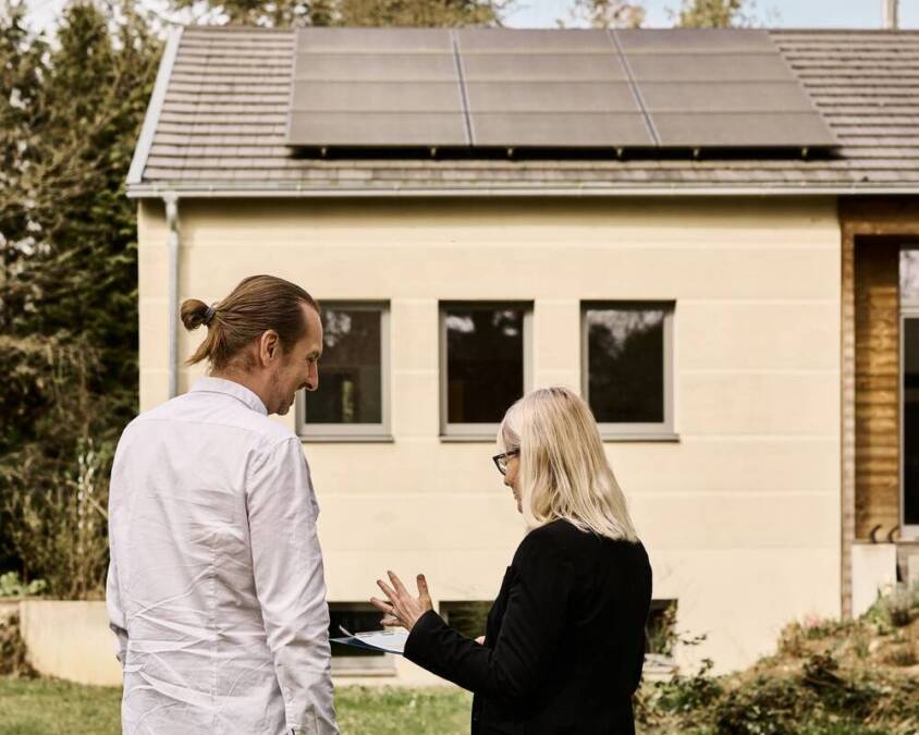 Zwei Energieberater*innen stehen vor einem Haus mit Solaranlage.
