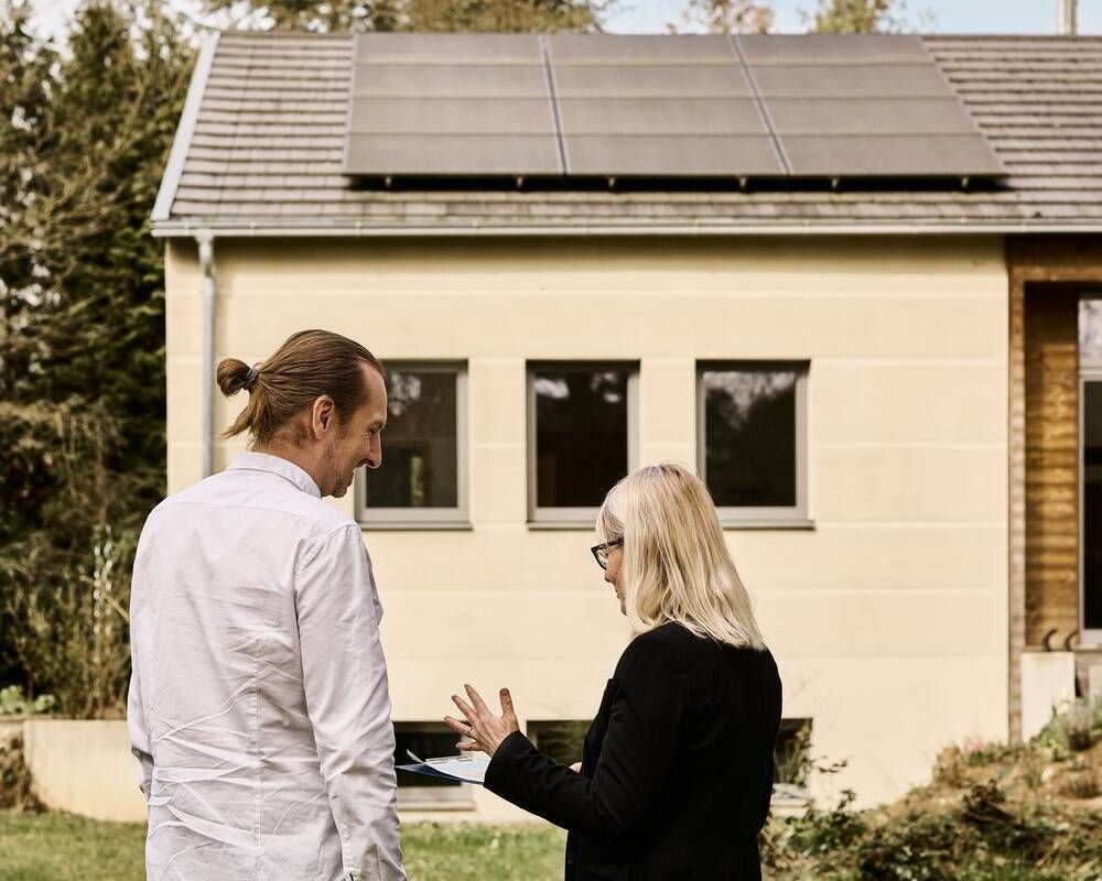 Zwei Energieberater*innen stehen vor einem Haus mit Solaranlage.