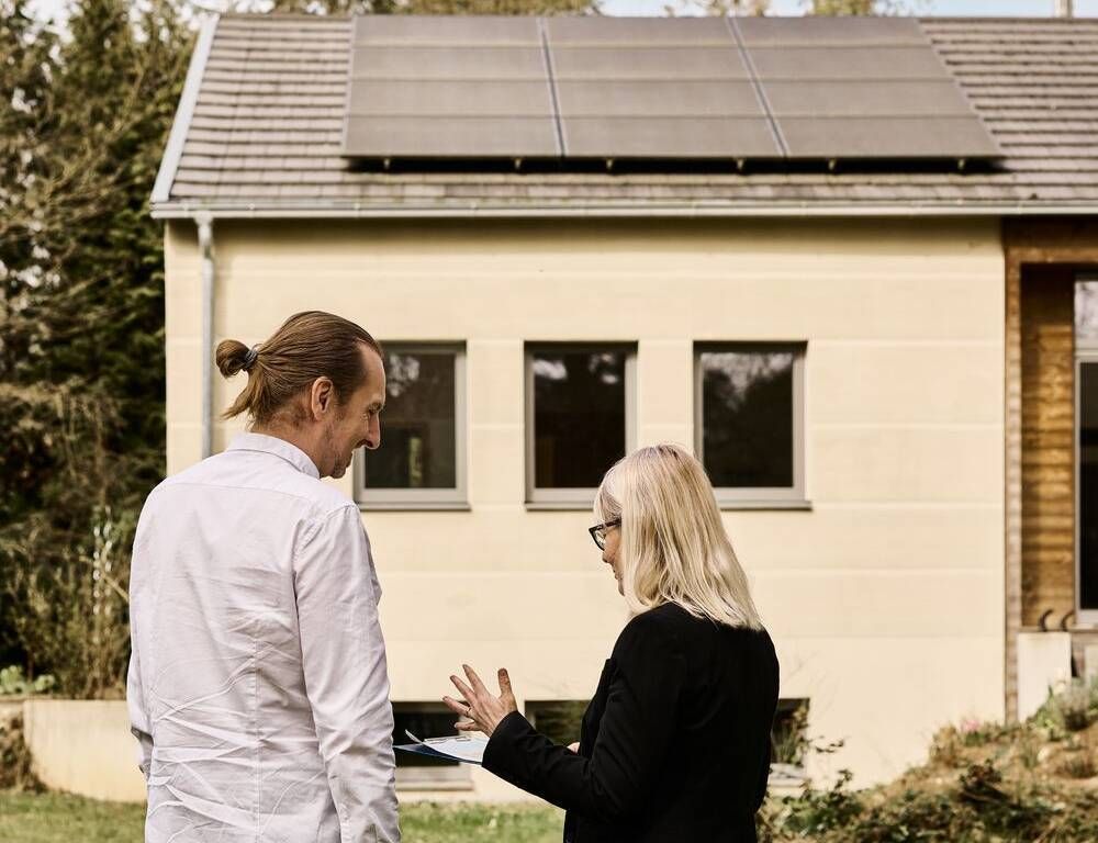 Zwei Energieberater*innen stehen vor einem Haus mit Solaranlage.