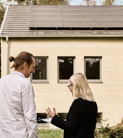 Zwei Energieberater*innen stehen vor einem Haus mit Solaranlage.