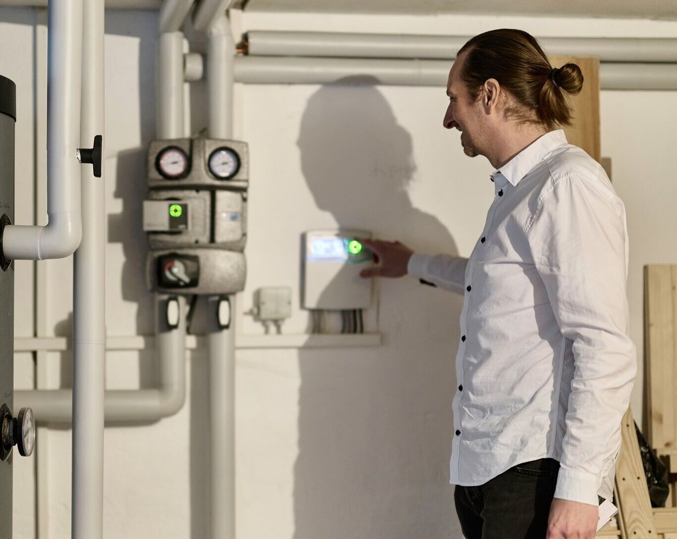 Mann steht in einem Heizungskeller neben einem Speicher und einer Pumpengruppe