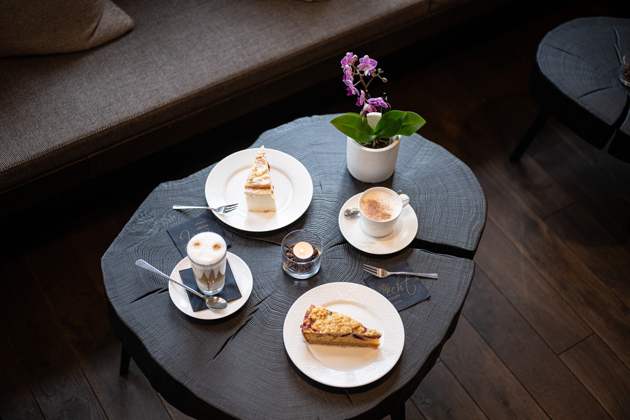Ein gedeckter Tisch mit zwei kunstvoll angerichteten Kuchenstücken und zwei Kaffeespezialitäten – ein einladender Moment zum Genießen in der Speisegalerie Fischen.