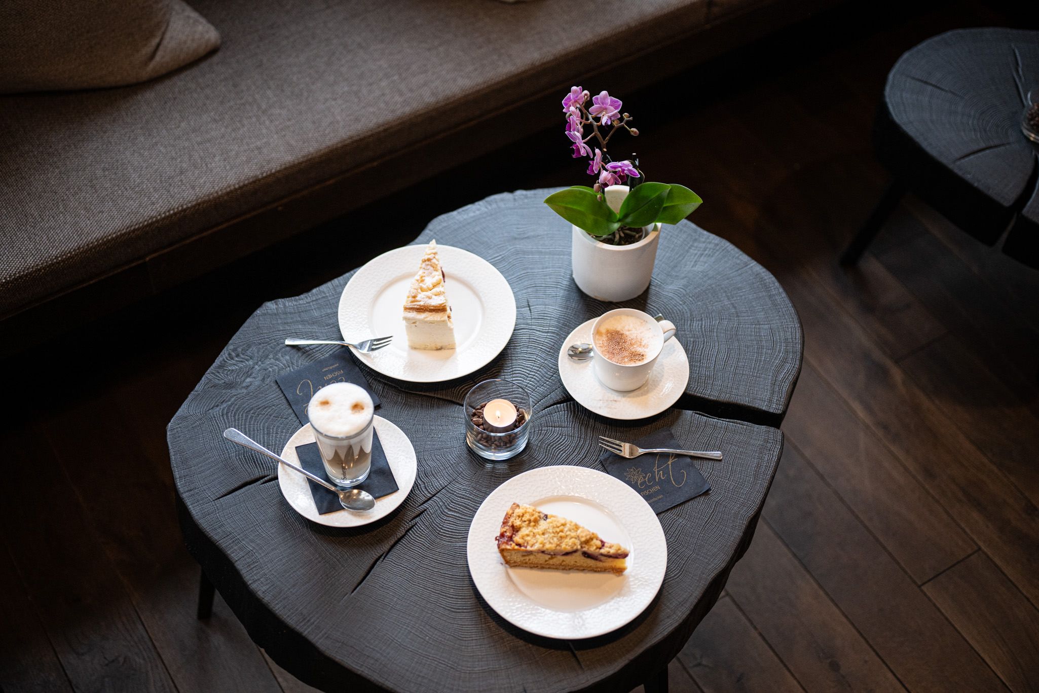 Ein gedeckter Tisch mit zwei kunstvoll angerichteten Kuchenstücken und zwei Kaffeespezialitäten – ein einladender Moment zum Genießen in der Speisegalerie Fischen.