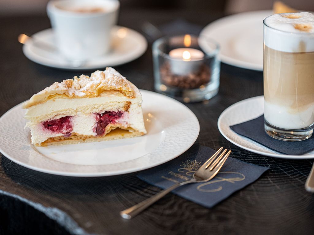 Nahaufnahme eines Stücks Kuchen neben einer dampfenden Tasse Kaffee – ein verlockendes Duo zum Genießen in der Speisegalerie Fischen.