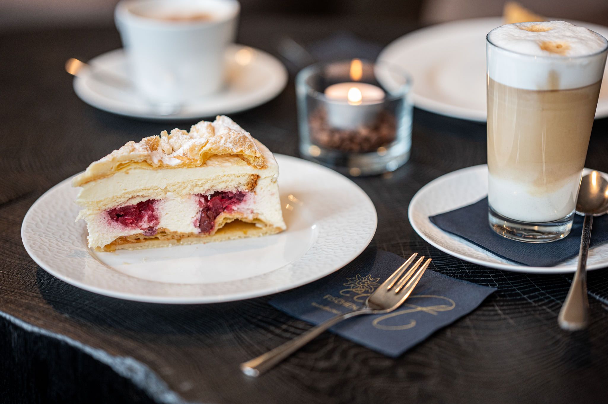 Nahaufnahme eines Stücks Kuchen neben einer dampfenden Tasse Kaffee – ein verlockendes Duo zum Genießen in der Speisegalerie Fischen.