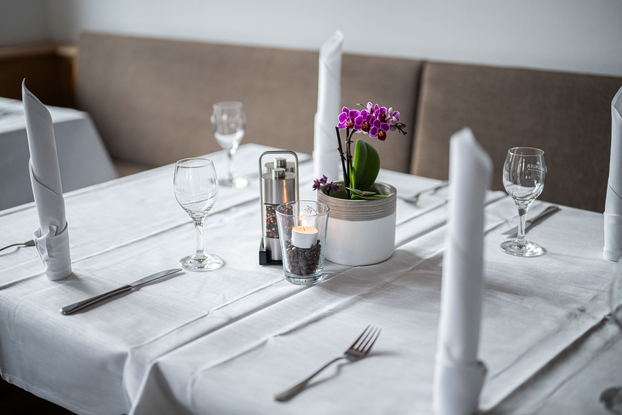 Minimalistisch gedeckter weißer Tisch mit einer kleinen Orchidee als eleganter Blickfang in der Mitte.