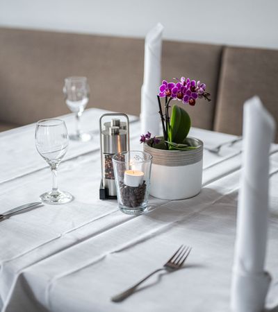 Minimalistisch gedeckter weißer Tisch mit einer kleinen Orchidee als eleganter Blickfang in der Mitte.