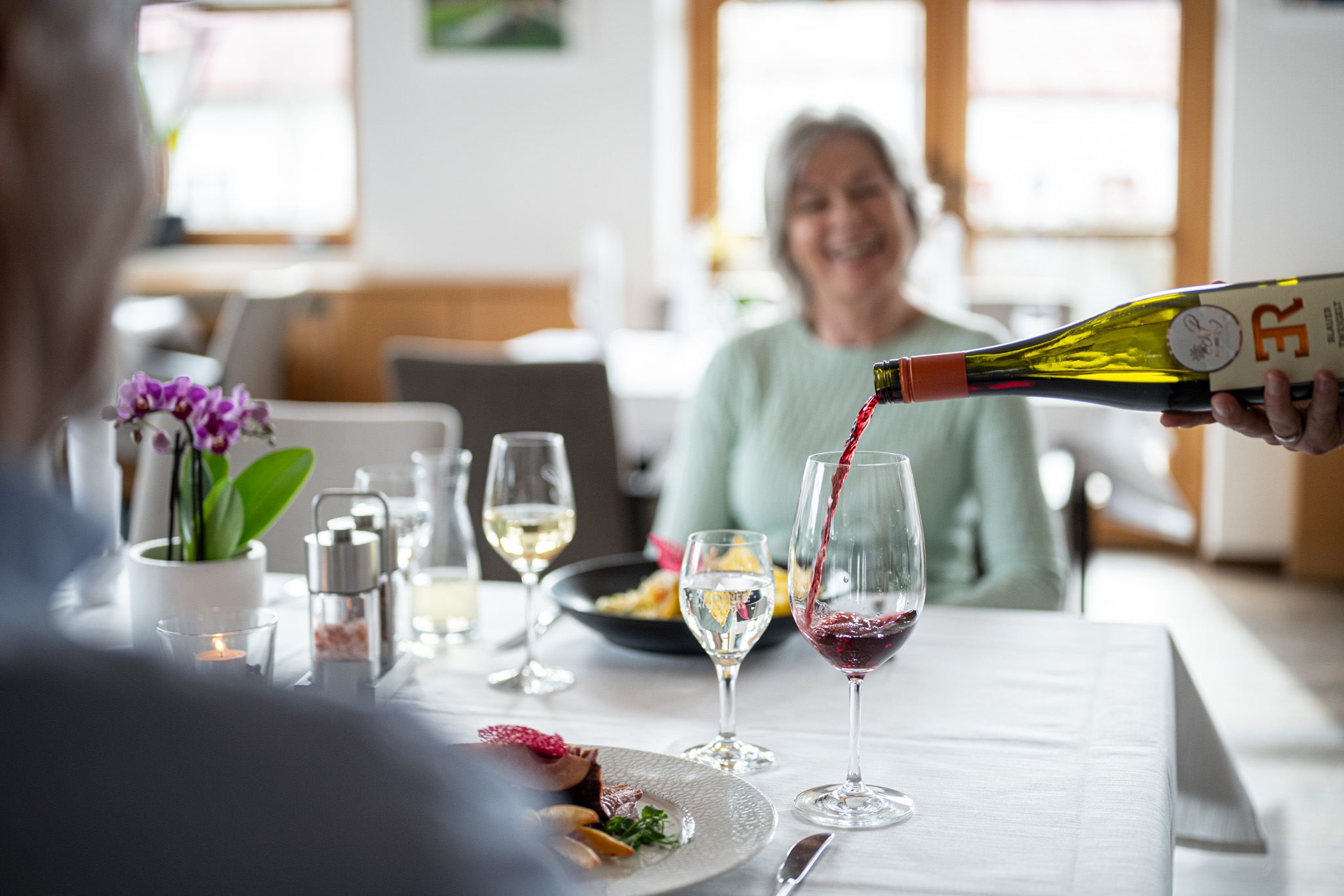 Ein Paar beim entspannten Mittagessen, vertieft in den Moment, während ihnen stilvoll Wein eingeschenkt wird – ein Ausdruck von Genuss, Nähe und Wohlfühlatmosphäre in der Speisegalerie Fischen.
