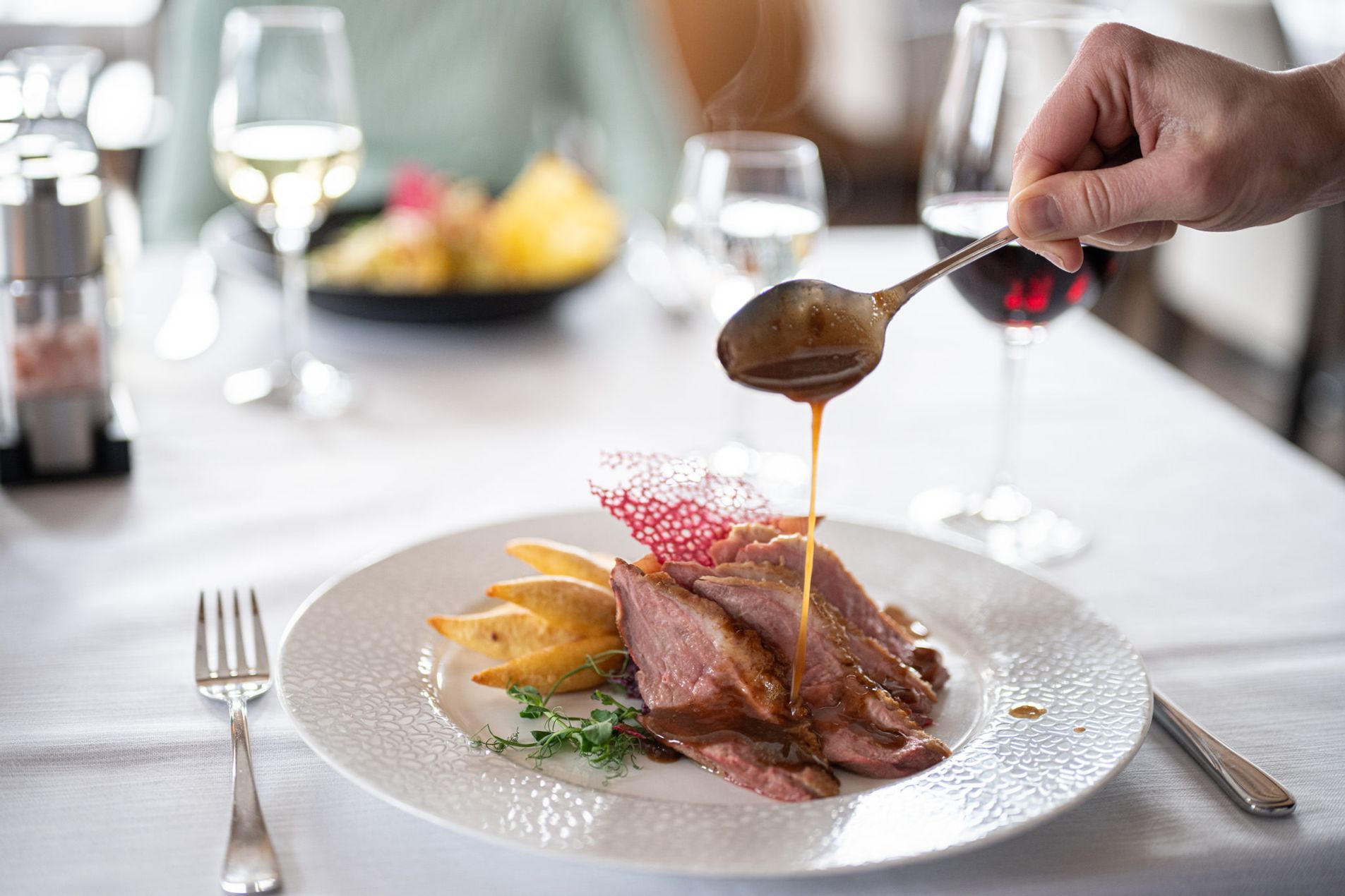 Zart rosa gegartes Fleisch, kunstvoll angerichtet, während eine feine Soße darüber gegossen wird – ein kulinarisches Highlight aus der Speisegalerie Fischen.