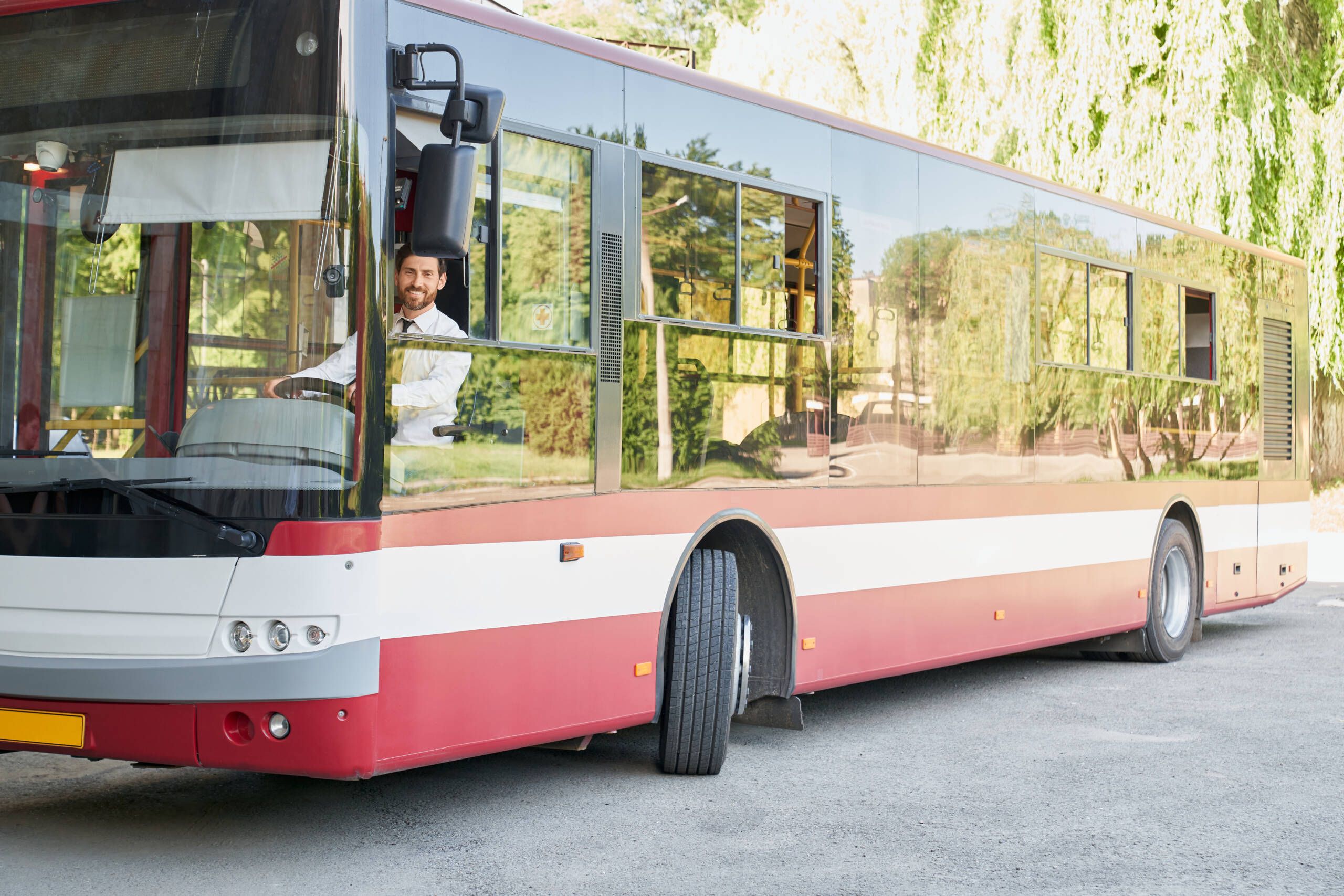 Eleganter Busfahrer sitzt lächelnd am Steuer eines Shuttle-Busses an einem sonnigen Tag – modernes Transportkonzept und freundlicher Service in der Stadt.