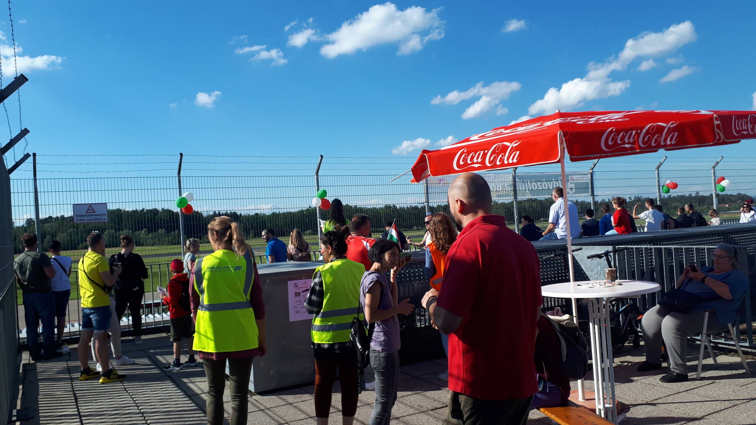 Visitors' terrace with lots of people, a chimney and people in high-visibility vests