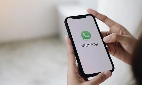 Handy in Hand. Whatsapp Logo auf Display.
