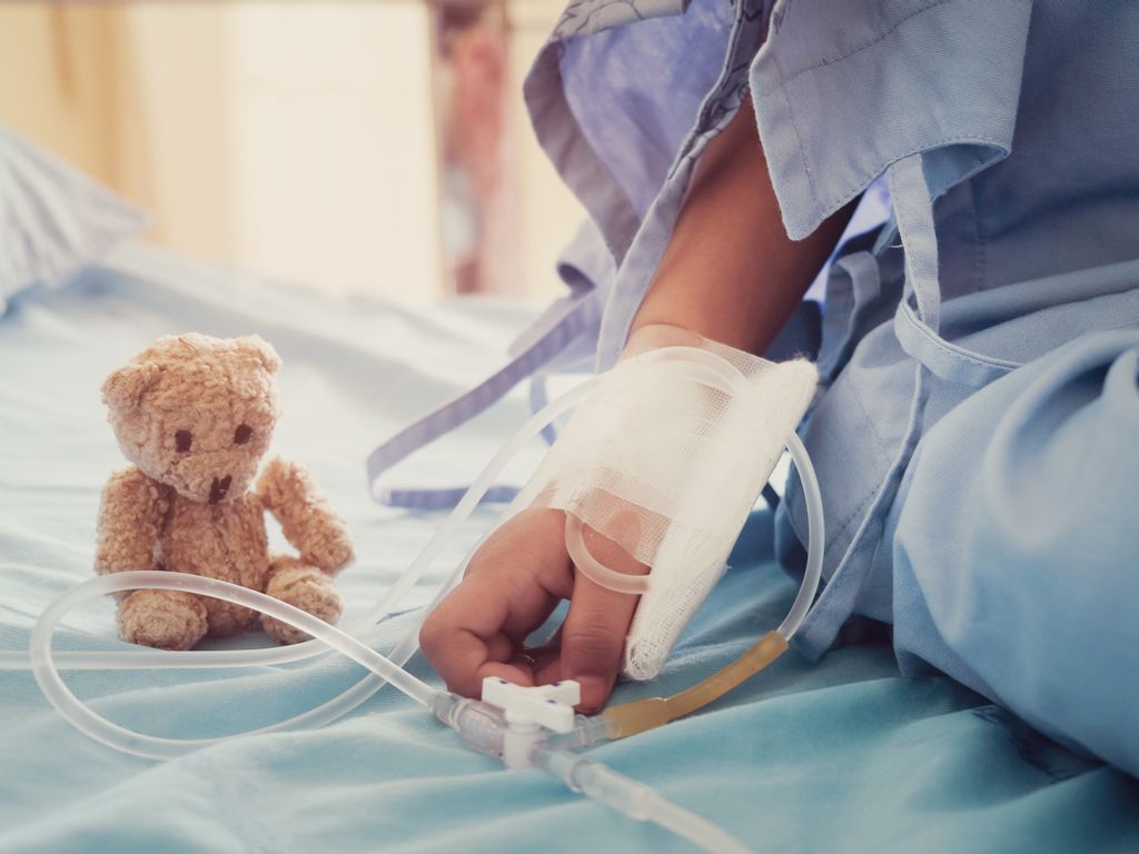 Soziales Engagement - Verbundene Kinderhand und Teddy auf Krankenhausbett