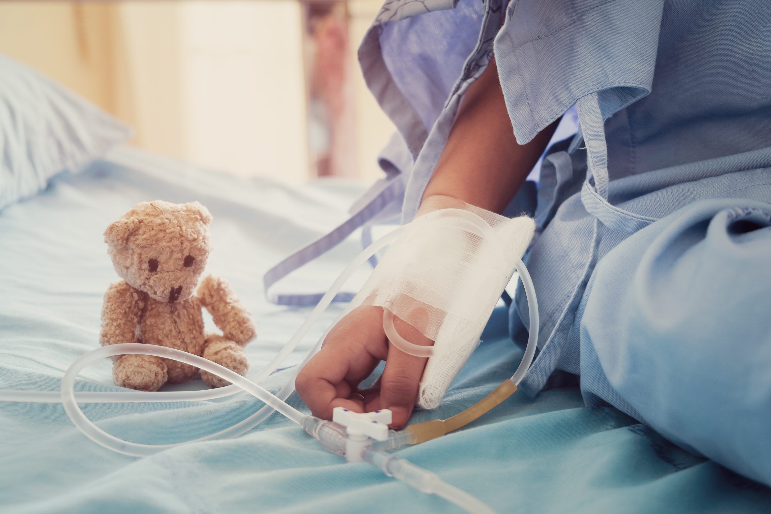 Soziales Engagement - Verbundene Kinderhand und Teddy auf Krankenhausbett