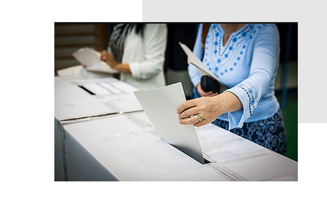 Teilnehmende stecken bei betriebliche Wahlen die Wahlunterlagen in Urnen.