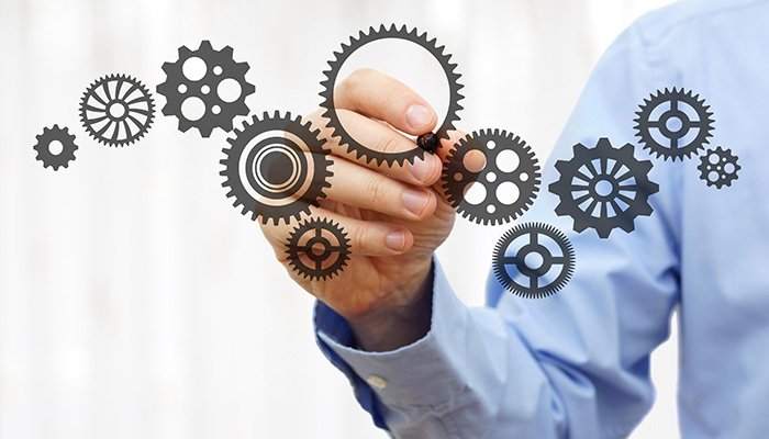 Ein Mann zeichnet im Rahmen der Fragebogenentwicklung Zahnräder an eine Glasscheibe.