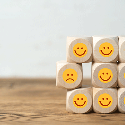 Mehrere Würfel sind übereinander gestapelt und haben Sticker mit teils lachenden und teils weinenden Smileys aufgeklebt. Diese symbolisieren die Kundenbefragung.