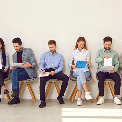 Sechs Menschen sitzen auf einem Stuhl und füllen eine Mitarbeiterbefragung aus.