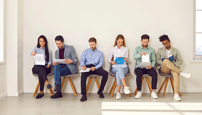 Sechs Menschen sitzen auf einem Stuhl und füllen eine Mitarbeiterbefragung aus.