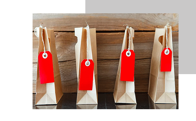 Preisforschungsmethoden sind unterschiedlich. Vier Papiertüten mit roten Preismarkierungen stehen vor einer Holzwand.