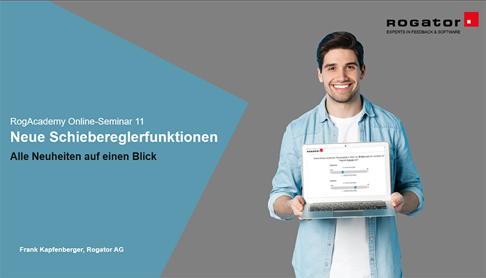 Ein Mann hält einen Laptop in der Hand und lacht in die Kamera