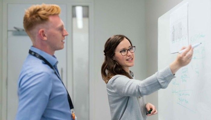 Eine Frau erklärt ihrem Kollegen am Whiteboard die Schnittstellenanbindung.