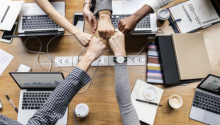 Der Team-Navigator stärkt die Zusammenarbeit. Ein Team sitzt an einem Tisch und gibt sich die Fäuste.