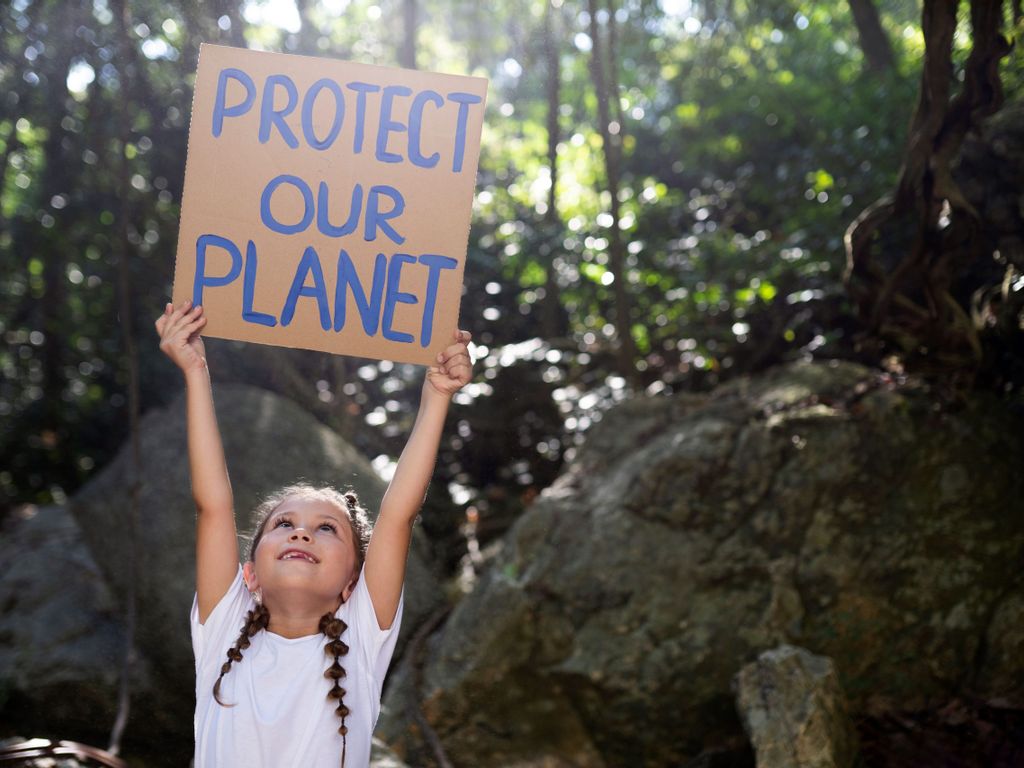 Kind hät Schild mit Aufschrift protect the planet hoch und fordert damit zu mehr Nachhaltigkeit auf